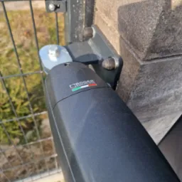 Szczegół montażu napędu bramy na słupku ogrodzeniowym, widoczne mocowanie oraz logo producenta.
