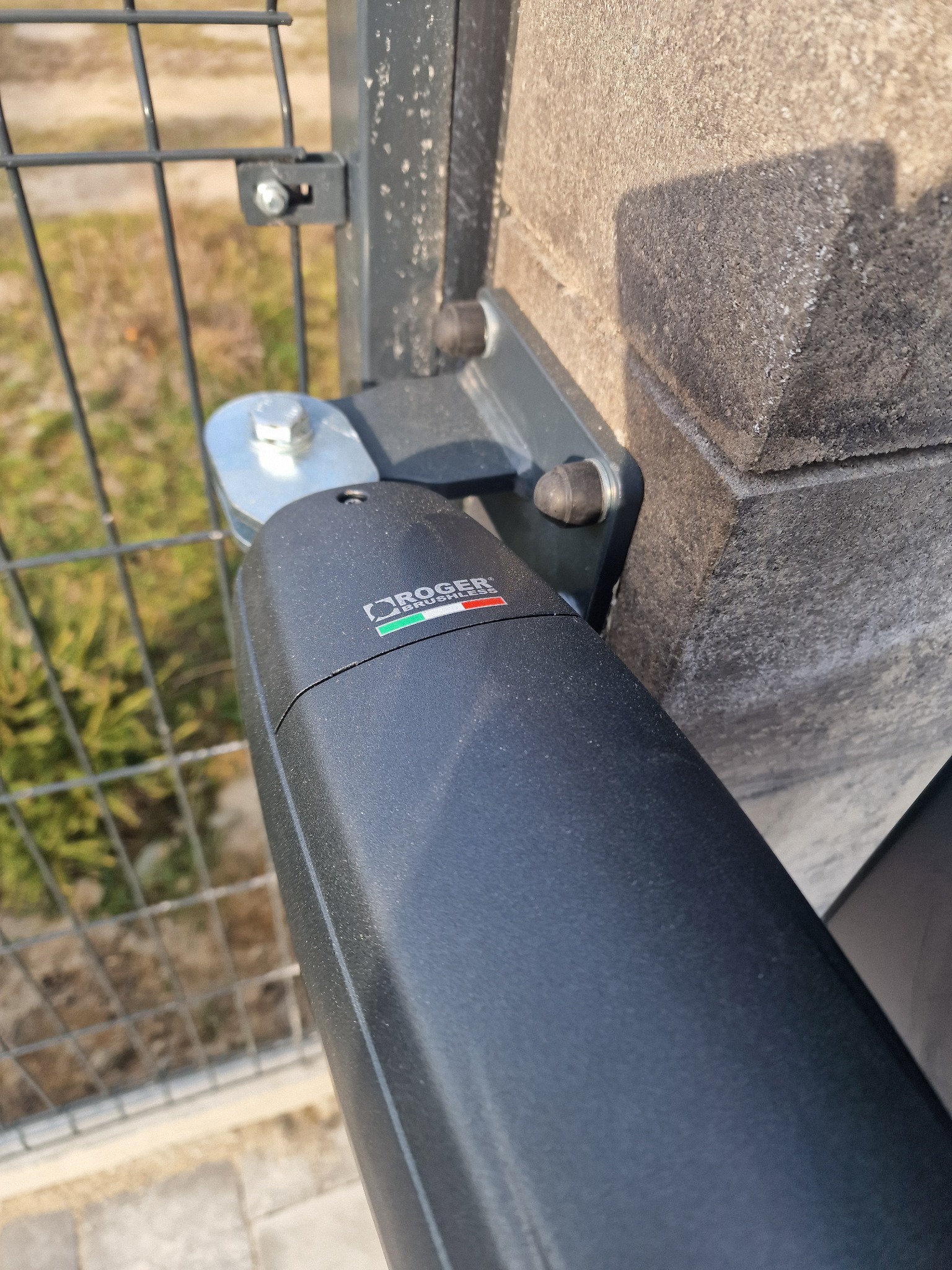 Szczegół montażu napędu bramy na słupku ogrodzeniowym, widoczne mocowanie oraz logo producenta.