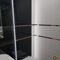 Remonty AZ - Nowoczesna łazienka z czarno-białymi płytkami, akcentami w kolorze miedzi i subtelnym oświetleniem LED. Minimalistyczny design z widocznym fragmentem toalety.