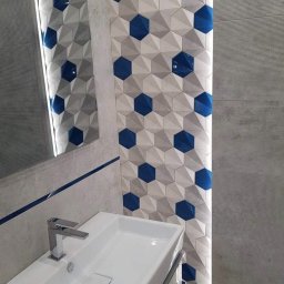 Remonty AZ - Nowoczesna łazienka: biała umywalka, lustro z podświetleniem i ściana z geometrycznymi płytkami w odcieniach szarości i niebieskiego, tworzącymi trójwymiarowy efekt.