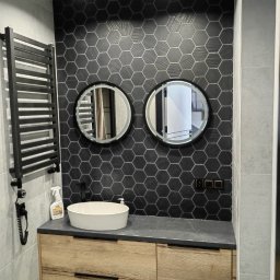 Remonty AZ - Nowoczesna łazienka w Kielcach: heksagonalne płytki, okrągłe lustra z podświetleniem LED, drewniana szafka pod umywalką i czarny grzejnik drabinkowy.
