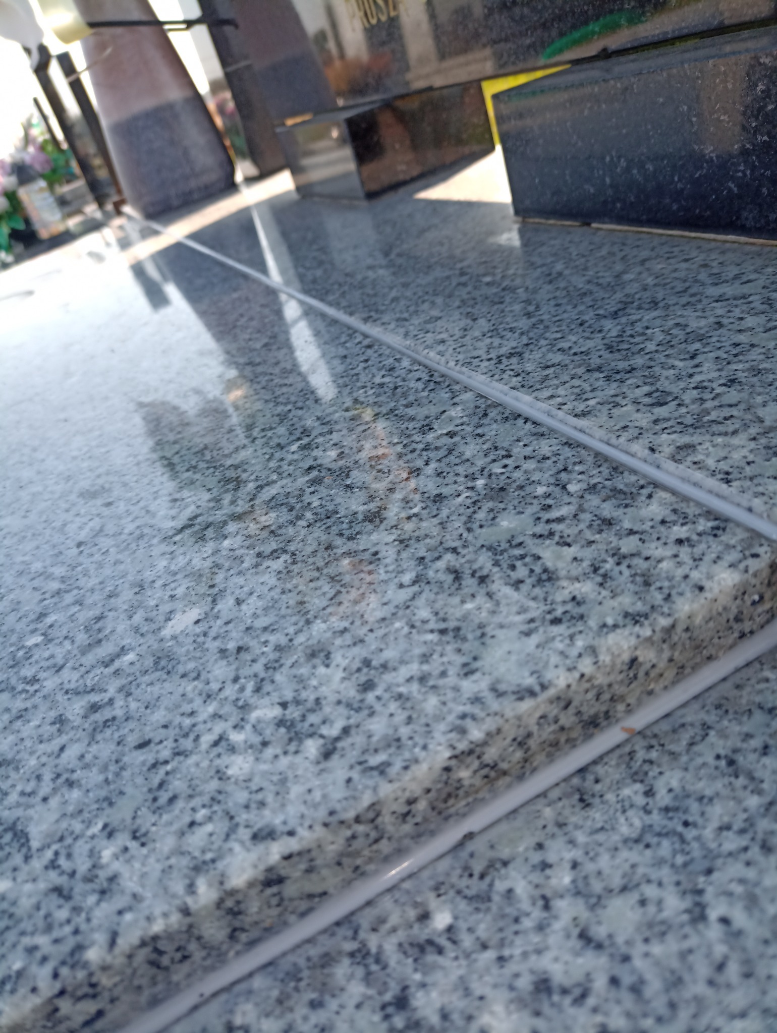 Szlifowany blat z granitu z widocznymi fugami, fragment nagrobka w tle. Ujęcie z bliska, ukazujące strukturę kamienia i precyzję wykonania.