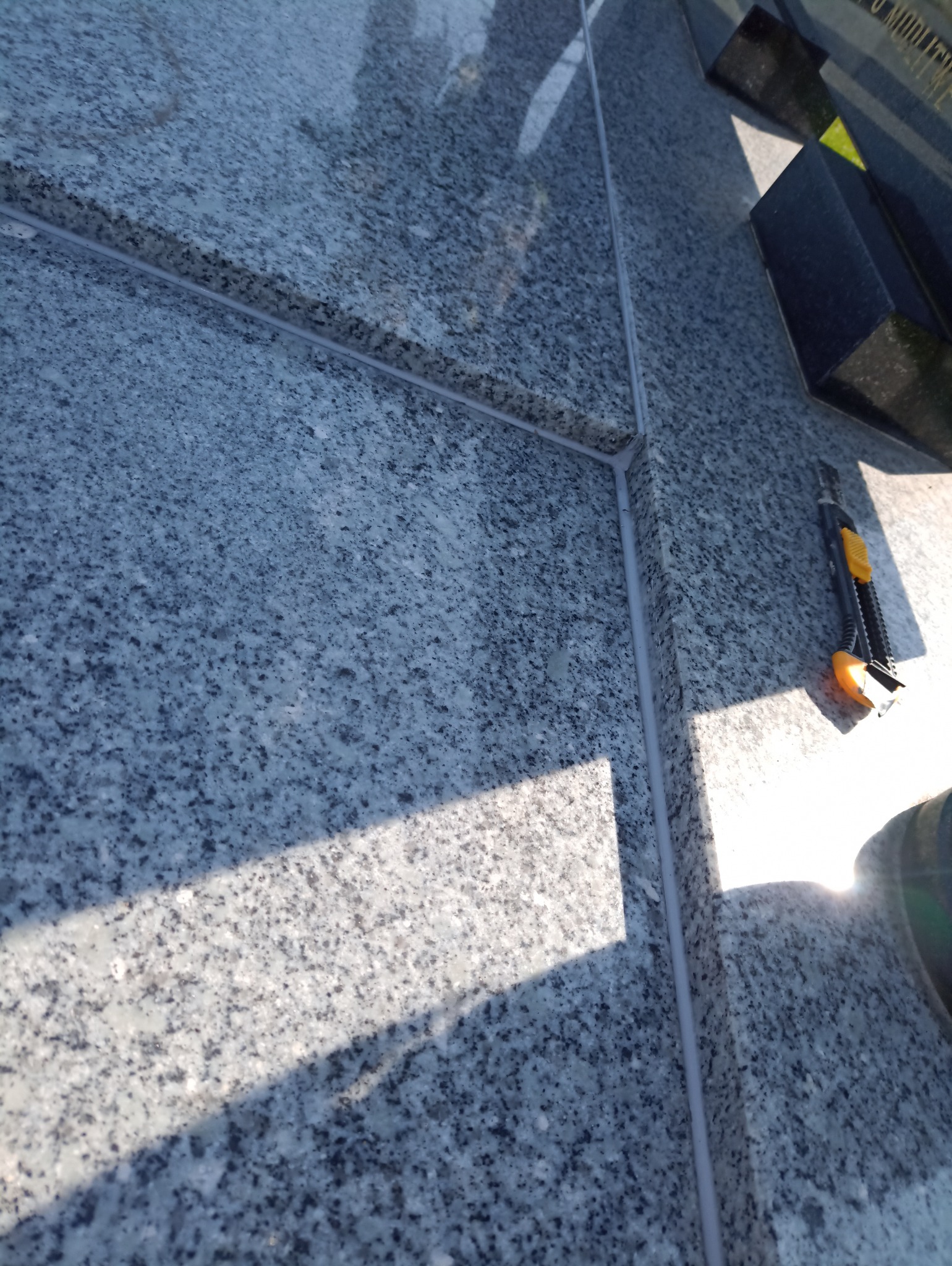 Szczegółowe ujęcie szarej, granitowej powierzchni z wypełnionymi spoinami i nożem do tapet, ukazujące precyzję wykonania i dbałość o detale.