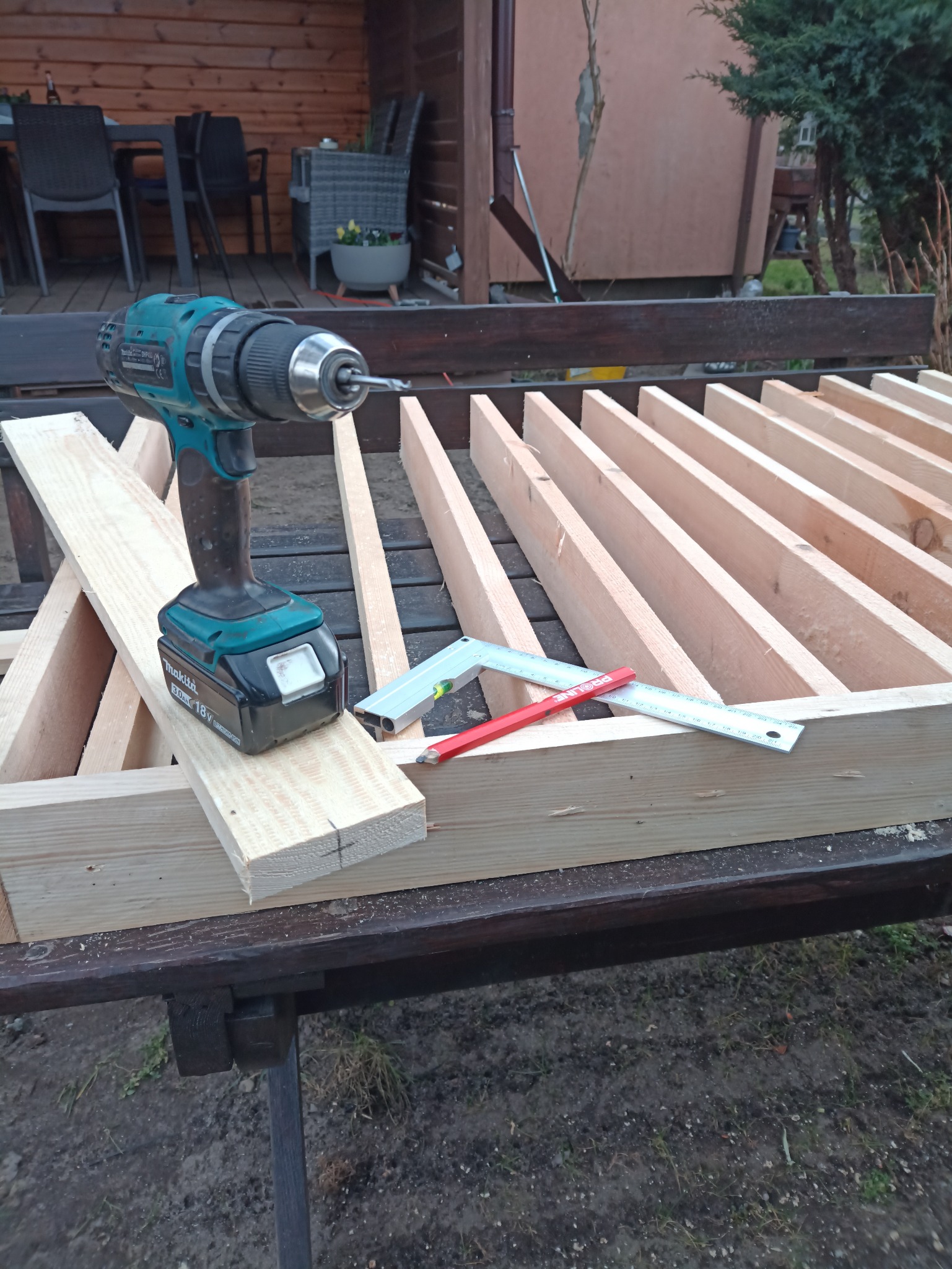 Drewniane elementy konstrukcyjne, wiertarka akumulatorowa i narzędzia pomiarowe na stole w Kaliszu. Przygotowanie do montażu konstrukcji drewnianej.