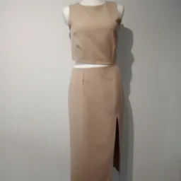 Beżowy komplet damski: krótki top i spódnica midi z rozcięciem, prezentowany na manekinie na tle szarej ściany.