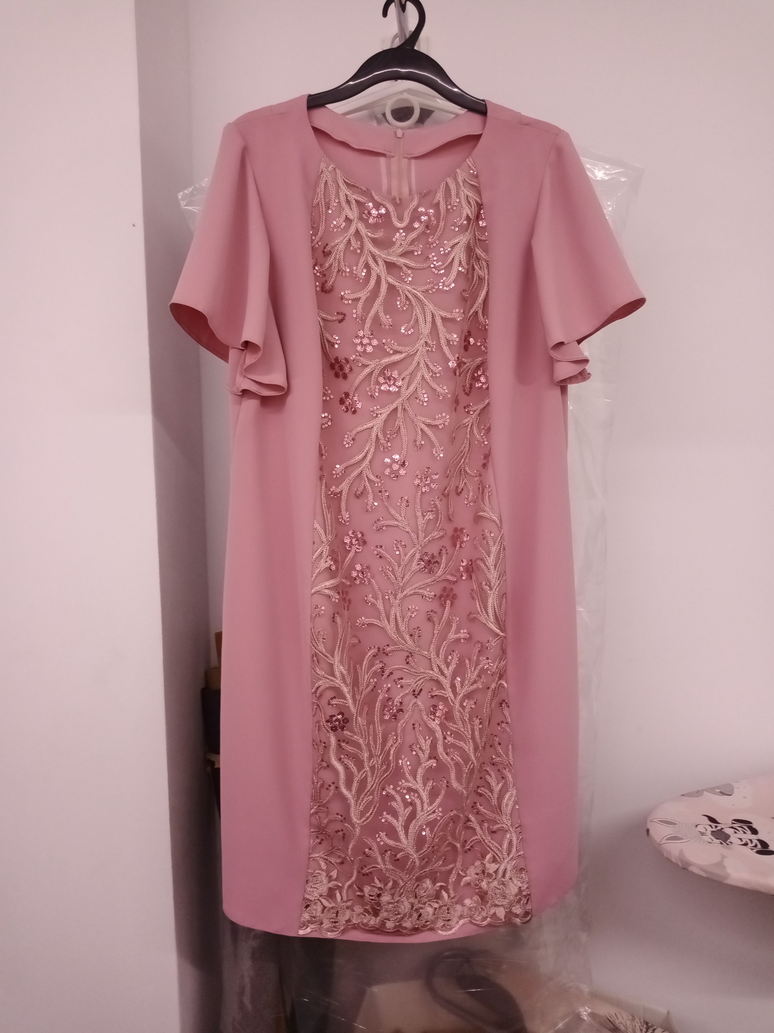 Różowa sukienka z dekoracyjnym haftem, wisząca na wieszaku, prezentowana przez krawca z Jeżowego.