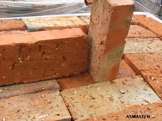 Ułożone cegły ceramiczne w odcieniach czerwieni i beżu, jedna ustawiona pionowo, widoczne ślady użytkowania i naturalna tekstura materiału, w tle folia ochronna.