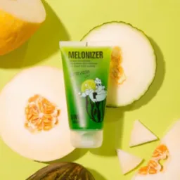 Tuba zielonego kremu Melonizer z ilustracją postaci pijaącej napój, otoczona połówkami i kawałkami melona na jasnozielonym tle.
