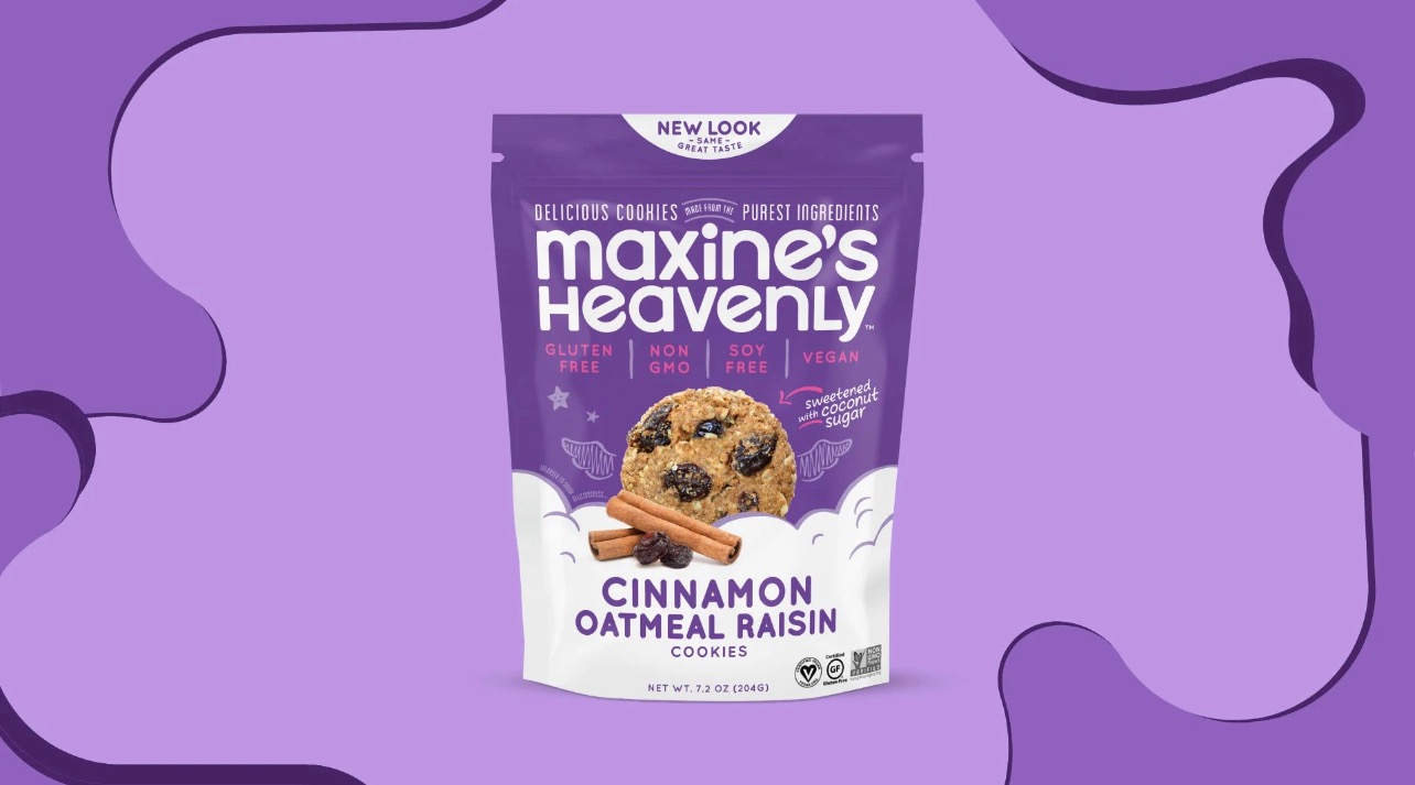 Fioletowe opakowanie ciasteczek cynamonowo-owsianych z rodzynkami marki Maxine's Heavenly, z widocznym ciasteczkiem i laskami cynamonu, na fioletowym tle z abstrakcyjnymi kształtami.