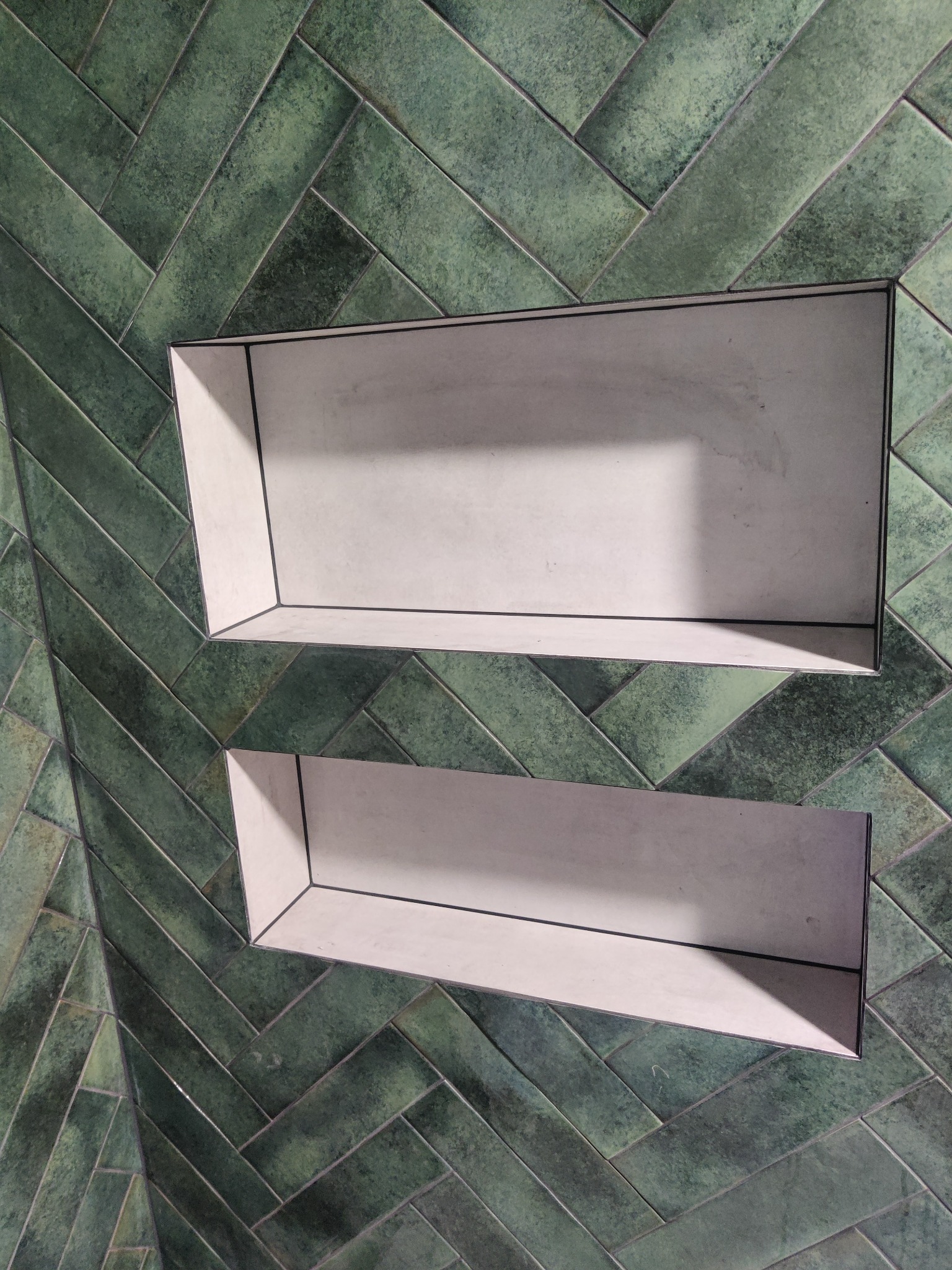 Dwie wnęki wyłożone jasnymi płytkami, wkomponowane w ścianę z zielonej, ułożonej w jodełkę glazury. Minimalistyczny design, precyzyjne wykończenie.