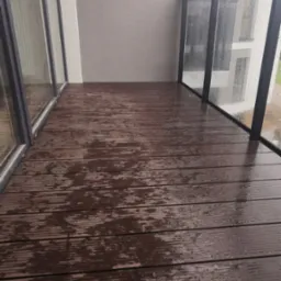 Wodoodporna, brązowa deska kompozytowa na balkonie z nowoczesną balustradą szklaną w deszczowy dzień.