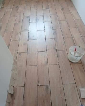 Układanie podłogi z płytek imitujących drewno, widoczne krzyżyki dystansowe, wiadro z zaprawą w rogu pomieszczenia.
