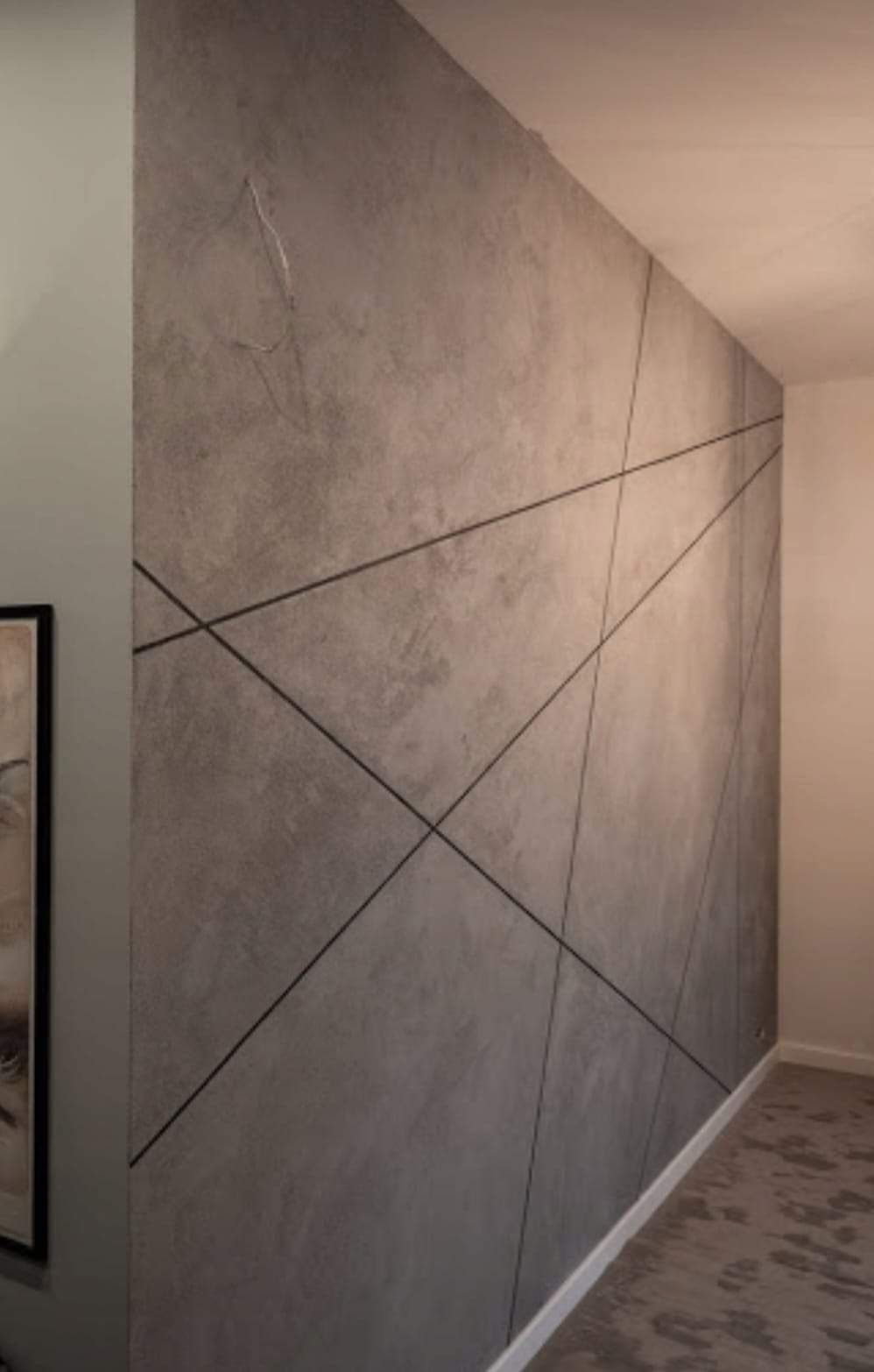 Ściana z szarego betonu architektonicznego z czarnymi, ukośnymi liniami tworzącymi geometryczny wzór, widoczne ślady po szpachlowaniu.