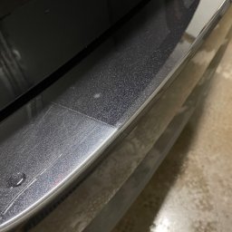 Pomydleni - Fragment karoserii samochodu z widocznymi śladami po myciu i kroplą wody na listwie, ukazujący detale lakieru i wykończenia.