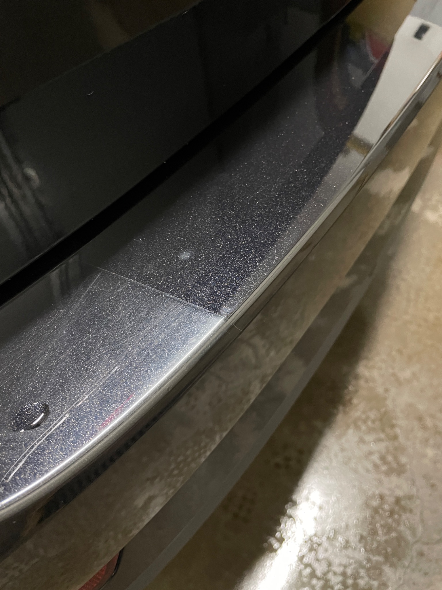 Fragment karoserii samochodu z widocznymi śladami po myciu i kroplą wody na listwie, ukazujący detale lakieru i wykończenia.