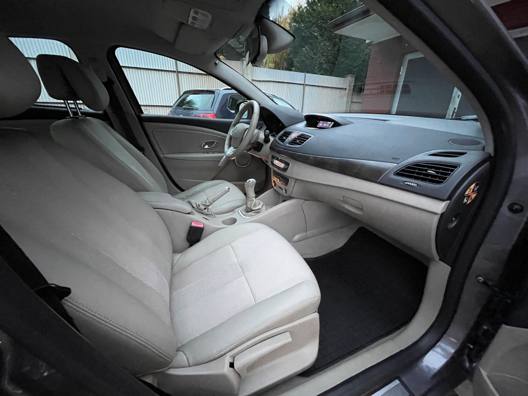 Wnętrze samochodu Renault Fluence z jasną tapicerką skórzaną, widok z otwartych drzwi pasażera, czarne dywaniki pod nogami.