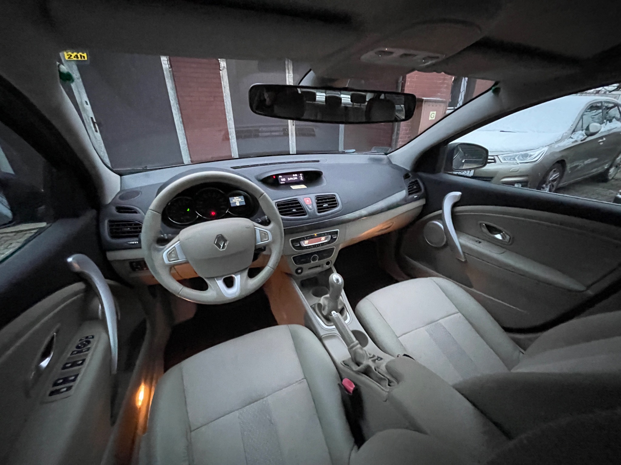Wnętrze samochodu Renault Megane z beżową tapicerką, widok z perspektywy pasażera, na zewnątrz zaparkowany inny samochód przykryty śniegiem.