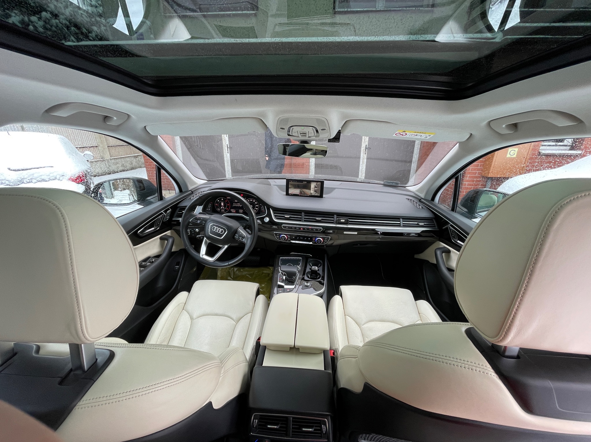 Wnętrze samochodu Audi Q7 z jasną skórzaną tapicerką, widok z tylnych siedzeń na deskę rozdzielczą i panoramiczny dach.