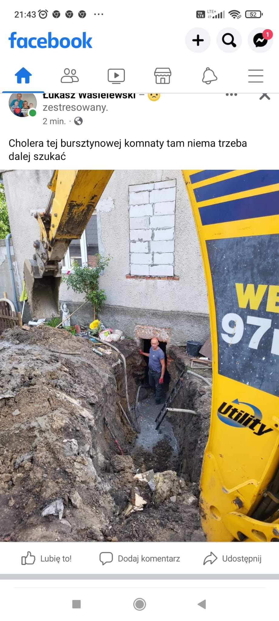 Głęboki wykop w ziemi przy budynku mieszkalnym, z pracownikiem w środku oraz fragmentem żółtej koparki na pierwszym planie, okno budynku zamurowane bloczkami.