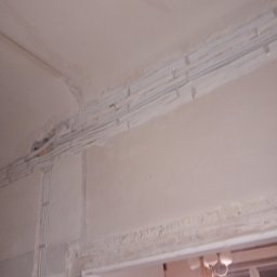 Ma-Gi Mariusz Gilewski Firma Handlowo-Usługowa - Białe rurki instalacji elektrycznej, przymocowane do sufitu i ściany w surowym stanie, widoczne przed tynkowaniem. Fragment widoku przez otwór drzwiowy.