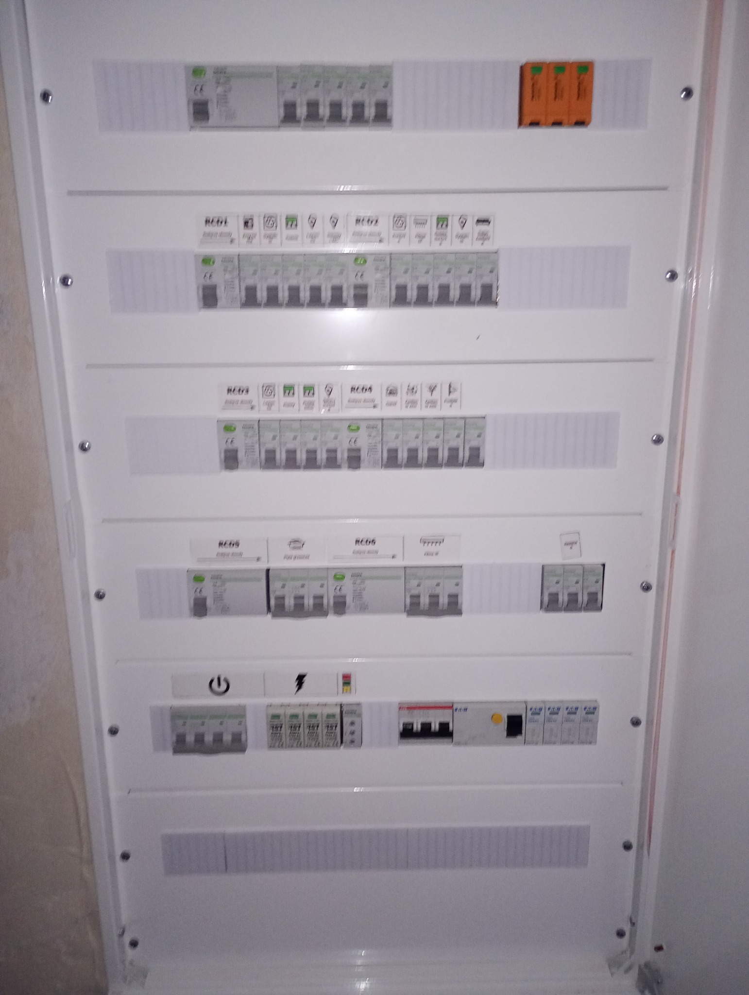 Rozdzielnica elektryczna z bezpiecznikami i oznaczeniami, zamontowana wewnątrz budynku, widok z bliska, oświetlenie dzienne.