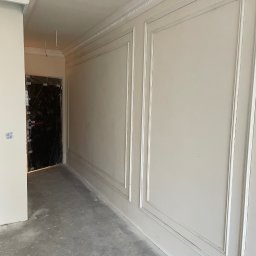 Przemek - Jasne wnętrze po szpachlowaniu z dekoracyjnymi listwami przy suficie i na ścianach. Drzwi zabezpieczone folią. Surowa podłoga.