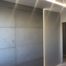 Przemek - Dekoracyjna ściana z betonu architektonicznego, podświetlona listwą LED, z widocznymi łączeniami płyt i subtelną fakturą, w nowoczesnym wnętrzu.