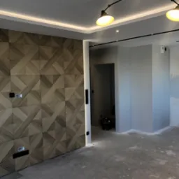 Nowoczesne wnętrze z dekoracyjną ścianą z paneli drewnianych o geometrycznym wzorze, oświetleniem LED i lampą sufitową w stylu industrialnym.