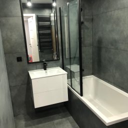 Przemek - Nowoczesna łazienka w szarościach: biała umywalka z szafką, czarne detale, przeszklona kabina nad wanną, duże szare płytki na ścianach i podłodze.