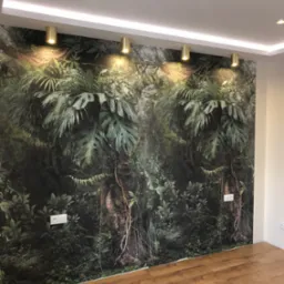 Ściana z fototapetą imitującą dżunglę, oświetlona złotymi lampami tubowymi. Widoczna drewniana podłoga i biały sufit z listwą LED. Nowoczesne wykończenie wnętrza.