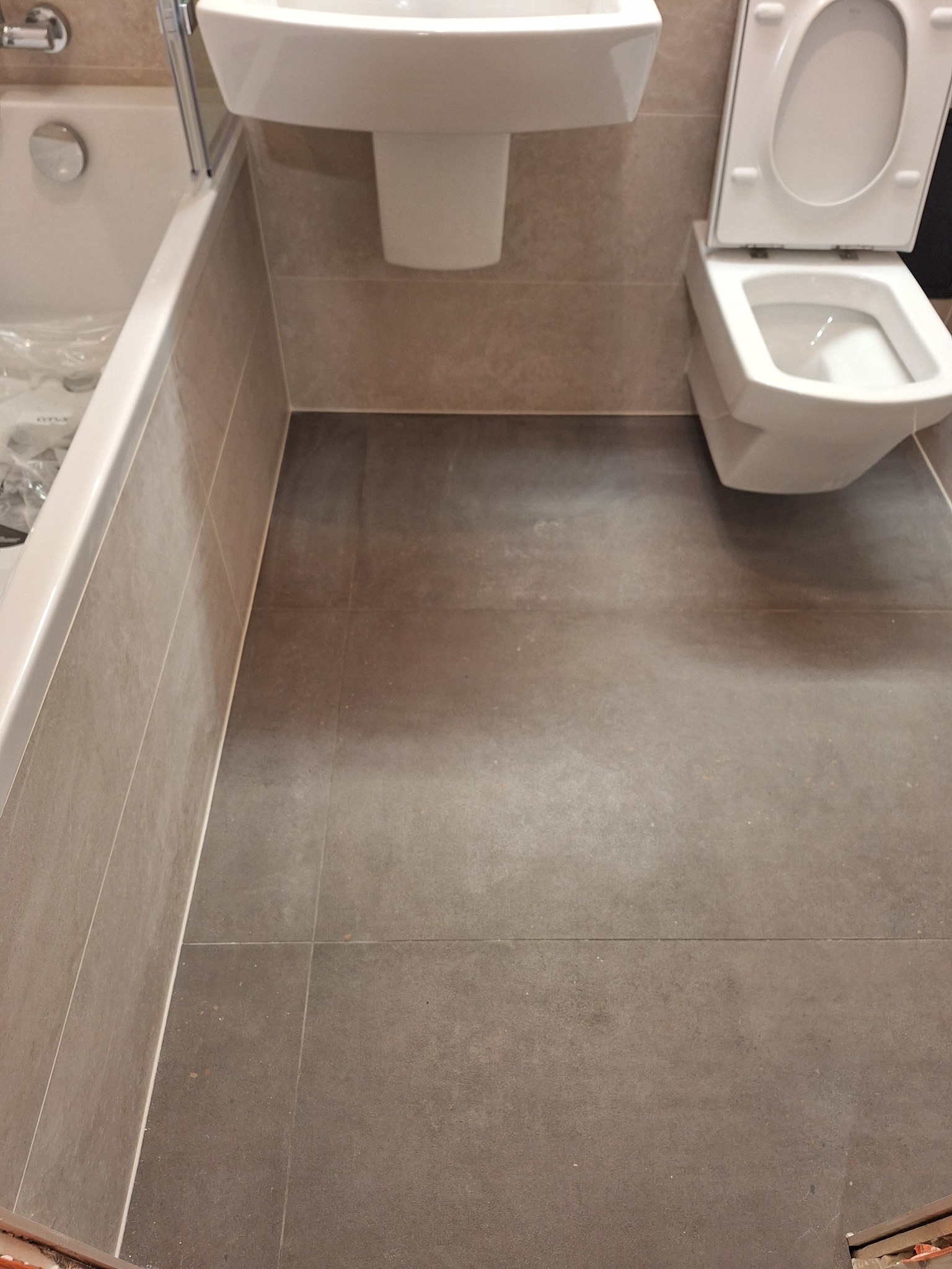 Wykończona łazienka w Katowicach z szarymi płytkami podłogowymi i ściennymi, białą umywalką oraz toaletą z otwartą klapą.