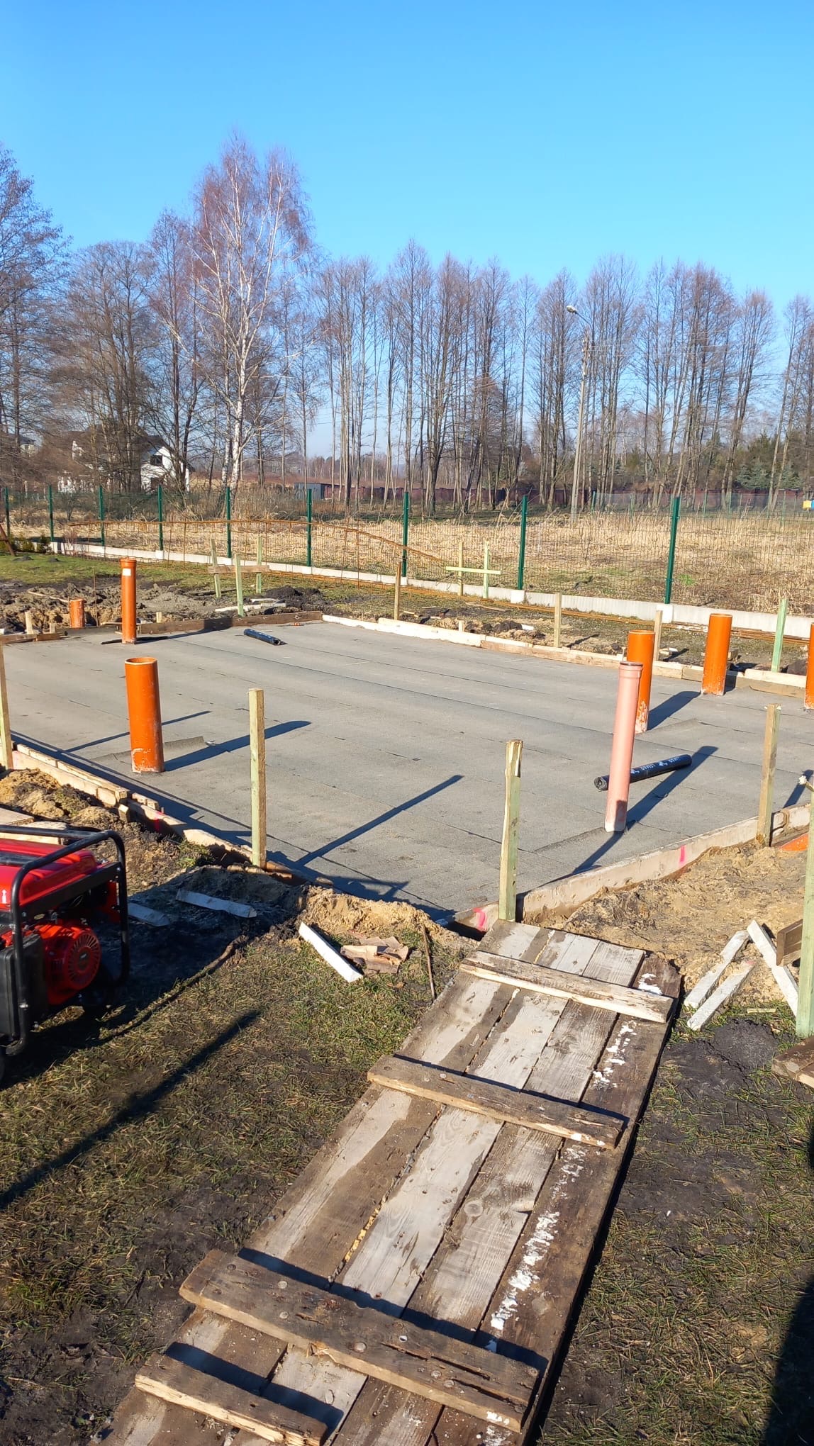 Przygotowany teren pod wylewkę fundamentów z deskowaniem, pionowymi rurami kanalizacyjnymi, agregatem prądotwórczym i prowizorycznym drewnianym pomostem dla pieszych.
