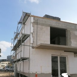 Firma Ogólnobudowlana - Budowa domu jednorodzinnego w trakcie ocieplania elewacji, widoczne rusztowanie, białe bloczki, fragment okna i izolacja termiczna.
