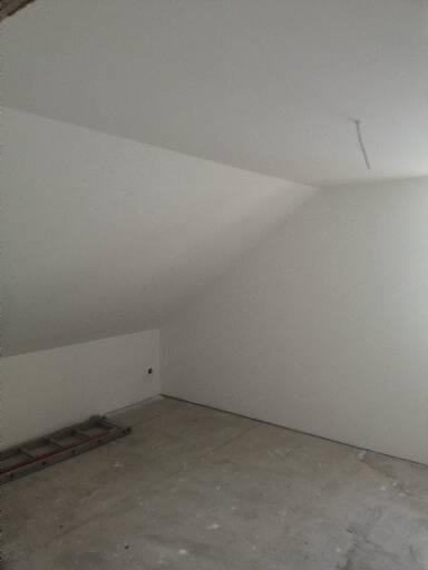 Poddasze po szpachlowaniu, przygotowane do dalszych prac wykończeniowych, z widoczną drabinką opartą o ścianę, sufit ze śladem po przewodzie.