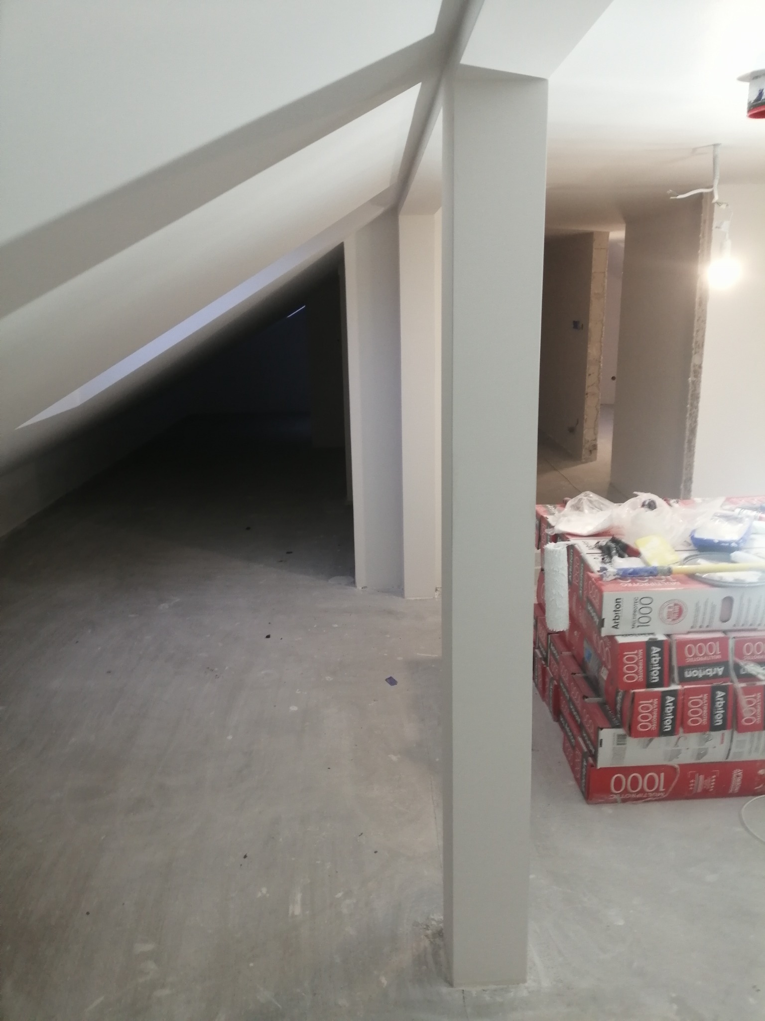 Adaptacja poddasza: ściany i sufit pomalowane na jasny kolor, widoczne przygotowane paczki paneli podłogowych Arbiton 1000 i narzędzia malarskie.