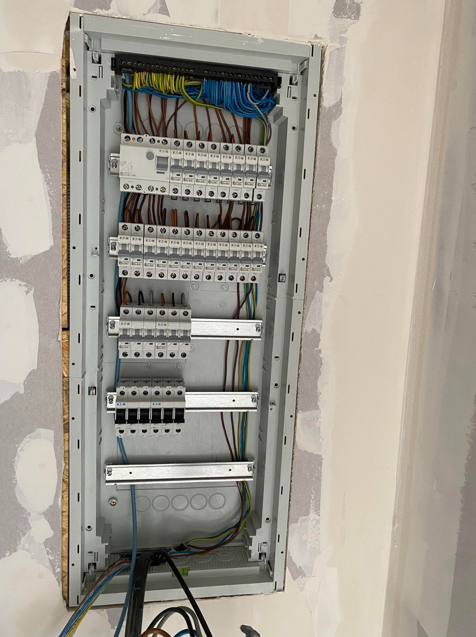 Rozdzielnica elektryczna marki Eaton zamontowana w ścianie podczas prac wykończeniowych, widoczne kable w różnych kolorach podłączone do bezpieczników.