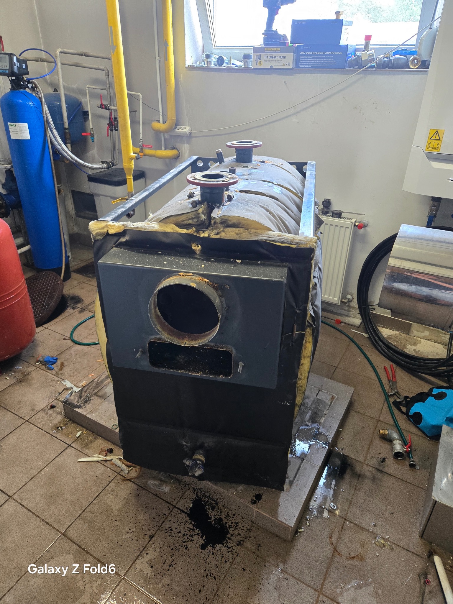 Demontaż starego pieca CO w kotłowni. Widoczne elementy instalacji hydraulicznej, narzędzia i pozostałości po pracach. Ujęcie z bliska, podkreślające etap wymiany.