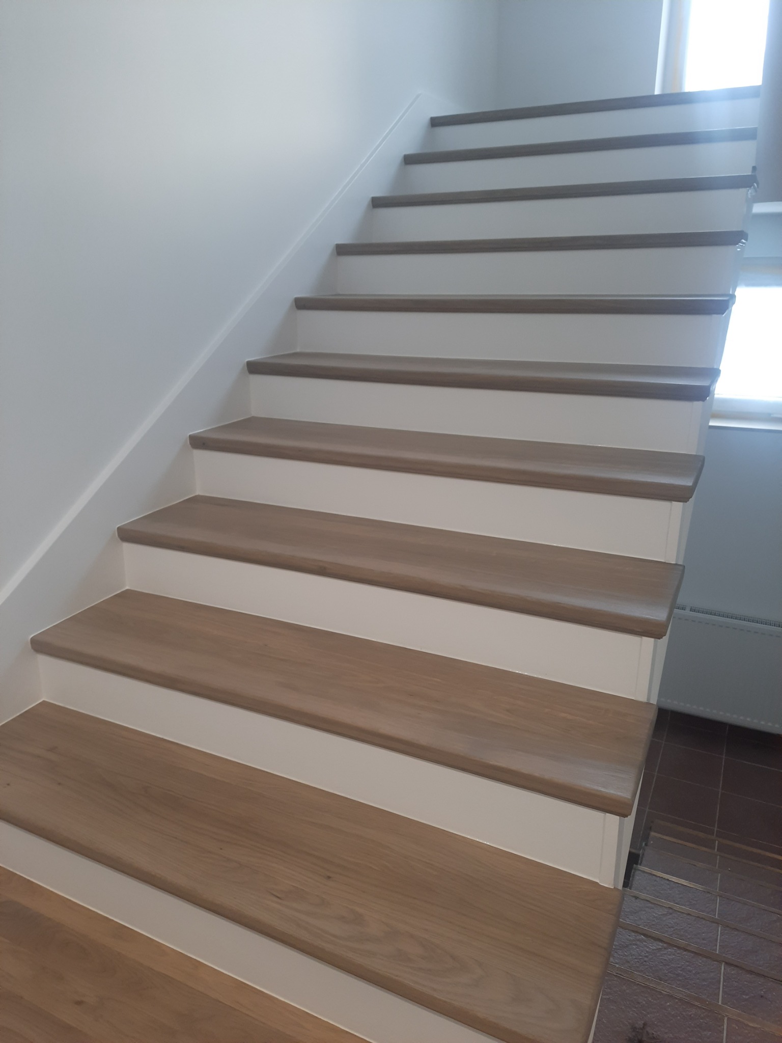 Jasne drewniane schody z białymi podstopnicami w nowoczesnym wnętrzu, widok z dołu, naturalne oświetlenie.