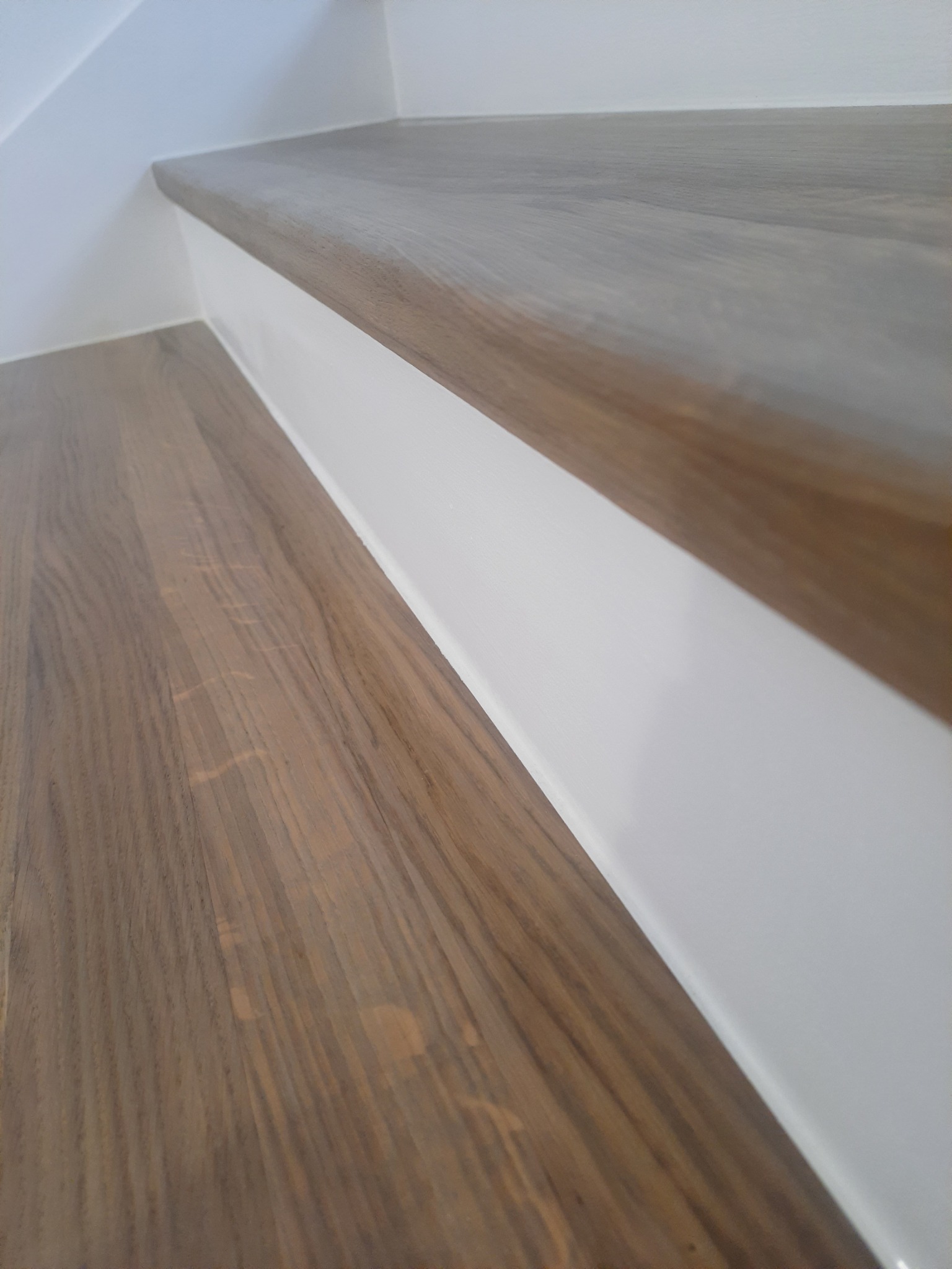 Detale wykończenia drewnianego stopnia schodów z białymi podstopnicami, widoczne delikatne usłojenie drewna i zaokrąglona krawędź stopnia.