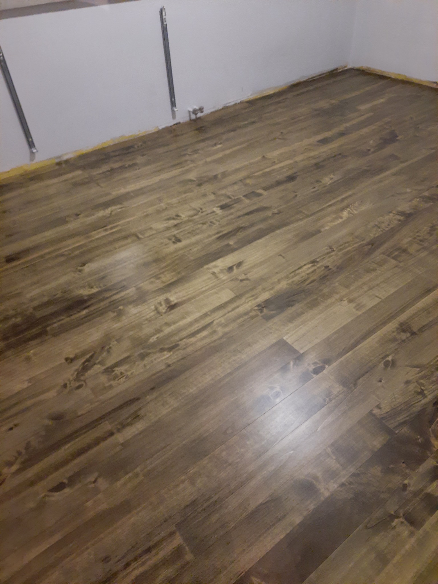 Ukończona podłoga z paneli o wzorze ciemnego drewna, widoczne listwy przypodłogowe i fragment ściany w rogu pomieszczenia.