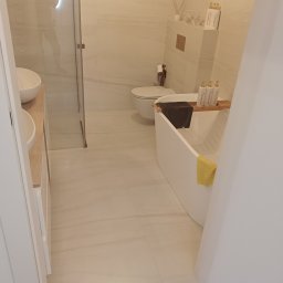 MZI Dmytro Shevchenko - Jasna łazienka z wanną, umywalką i kabiną prysznicową. Płytki imitujące marmur na ścianach i podłodze. Minimalistyczny design z akcentami w kolorze drewna.