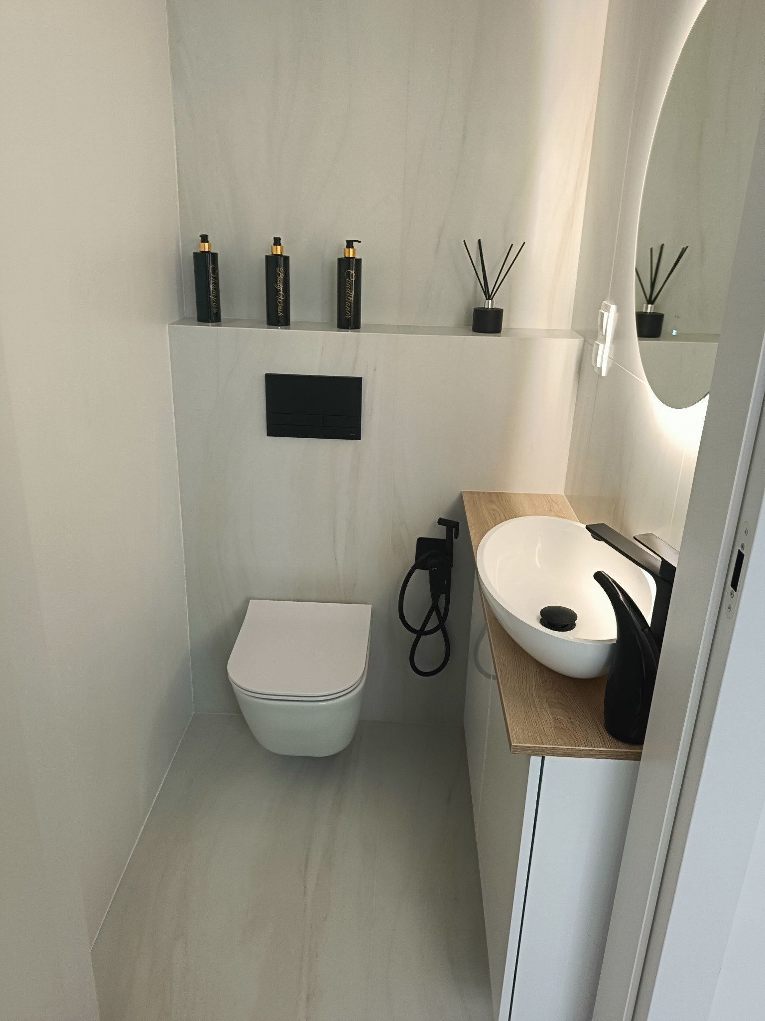 Nowoczesna, minimalistyczna łazienka po remoncie w Bydgoszczy. Białe płytki imitujące marmur, podwieszana toaleta, owalna umywalka nablatowa i czarna armatura.