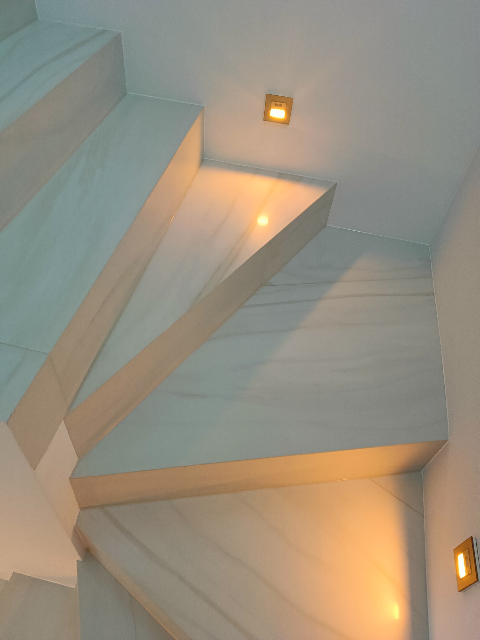 Marmurowe schody z podświetleniem LED w nowoczesnym wnętrzu. Ujęcie od dołu, ukazujące detale wykończenia i ciepłe światło lamp.