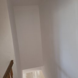 Adrian Sroka - Świeżo pomalowane, jasne ściany klatki schodowej z drewnianą balustradą, widoczne ślady szpachlowania na ścianie w tle.