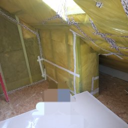 Adrian Sroka - Poddasze w trakcie prac izolacyjnych, widoczna wełna mineralna zabezpieczona folią i taśmą, surowa podłoga z płyt OSB, fragment ściany z przytwierdzoną łatą.