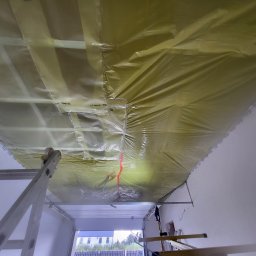 Adrian Sroka - Montaż folii paroizolacyjnej na metalowym ruszcie poddasza, widoczna drabina i fragment ściany