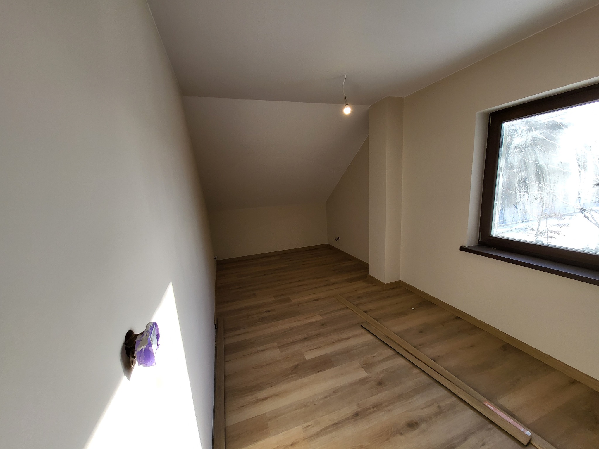 Poddasze po remoncie: świeżo pomalowane ściany w odcieniach beżu, ułożona podłoga z paneli winylowych, widoczna puszka elektryczna zabezpieczona folią malarską i fragmenty nieułożonych paneli...