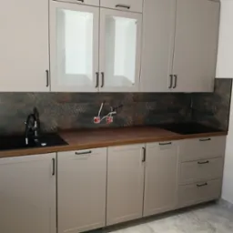 Kuchnia z beżowymi szafkami, czarnym zlewozmywakiem i brązową deską, widoczne gniazdka elektryczne przed montażem.