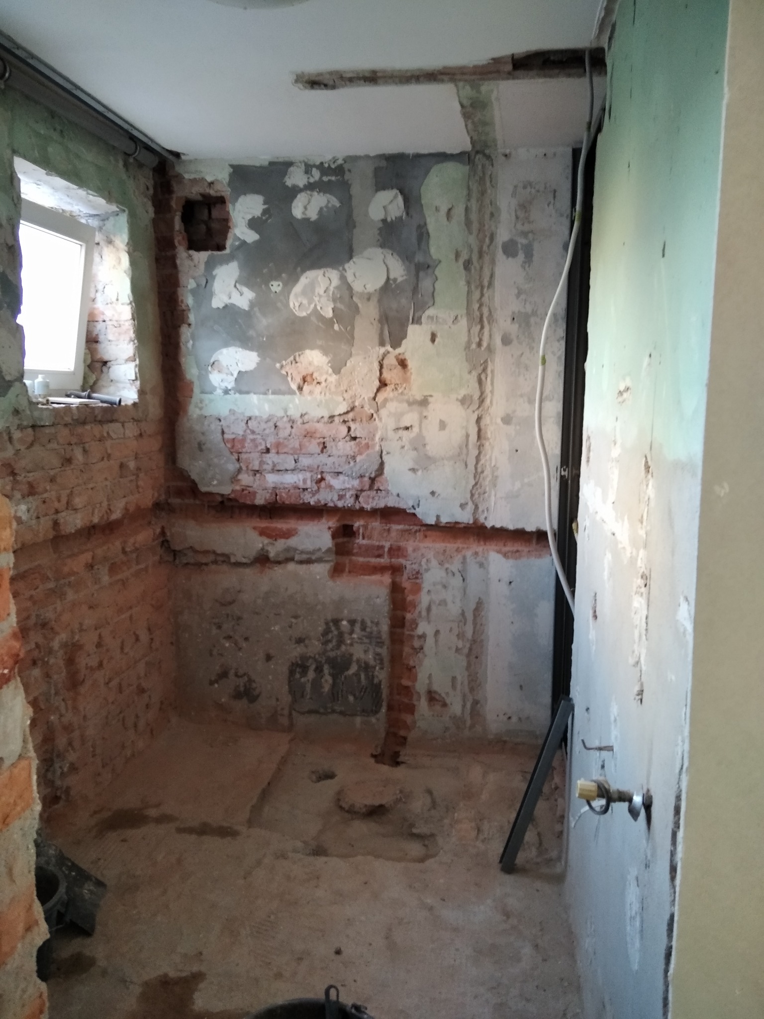 Łazienka w trakcie remontu: odsłonięta cegła, częściowo otynkowane ściany, widoczne instalacje, przygotowanie do dalszych prac wykończeniowych.