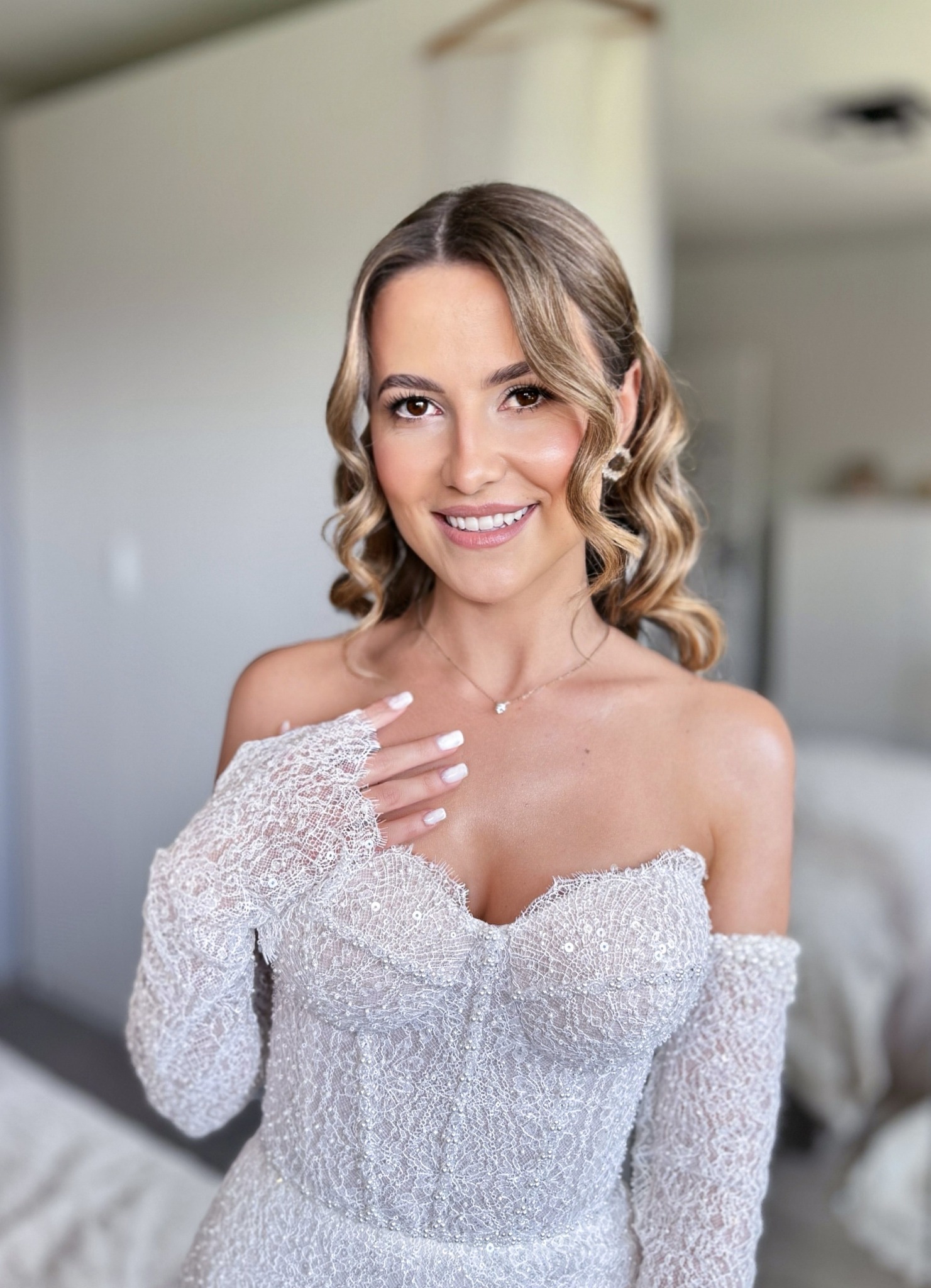 Uśmiechnięta kobieta w koronkowej sukni z delikatnym makijażem i upiętymi włosami. Subtelna biżuteria podkreśla stylizację. Idealne uczesanie na ważną uroczystość.